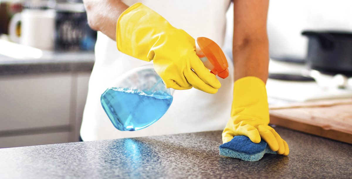 Person disinfecting kitchen counter top with cleaning solution