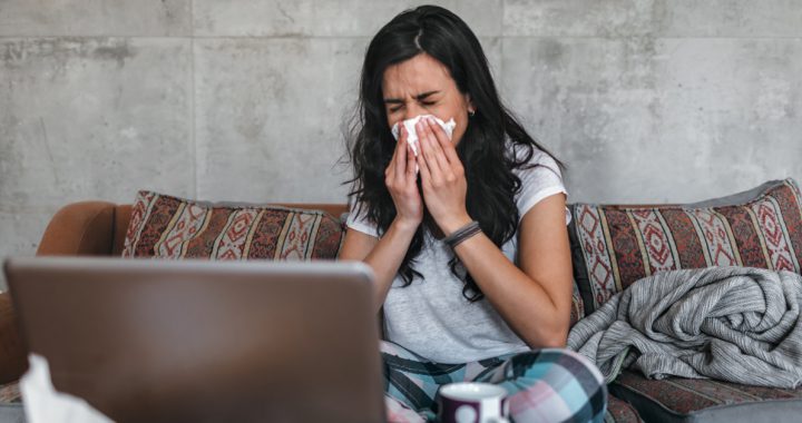 Woman blowing her nose while looking at computer screen.