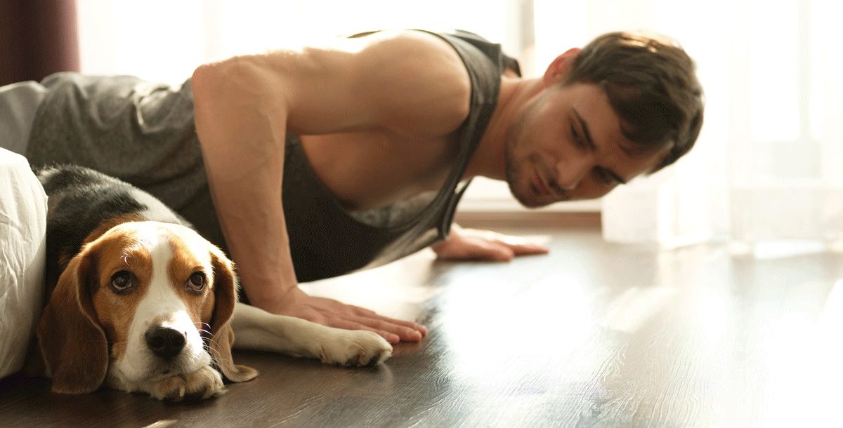 A man working out at home during COVID-19 with his dog.