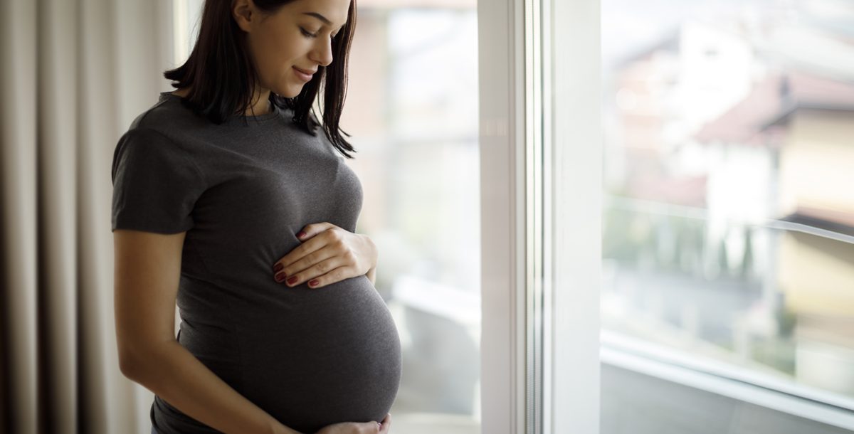 Pregnant women holding her baby bump and looking out the window