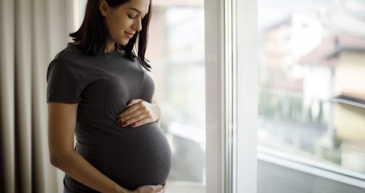 Pregnant women holding her baby bump and looking out the window