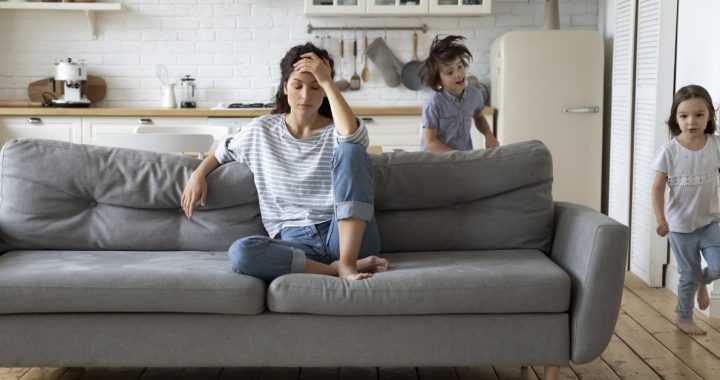 A mom taking a moment to herself on the couch while kids run around.