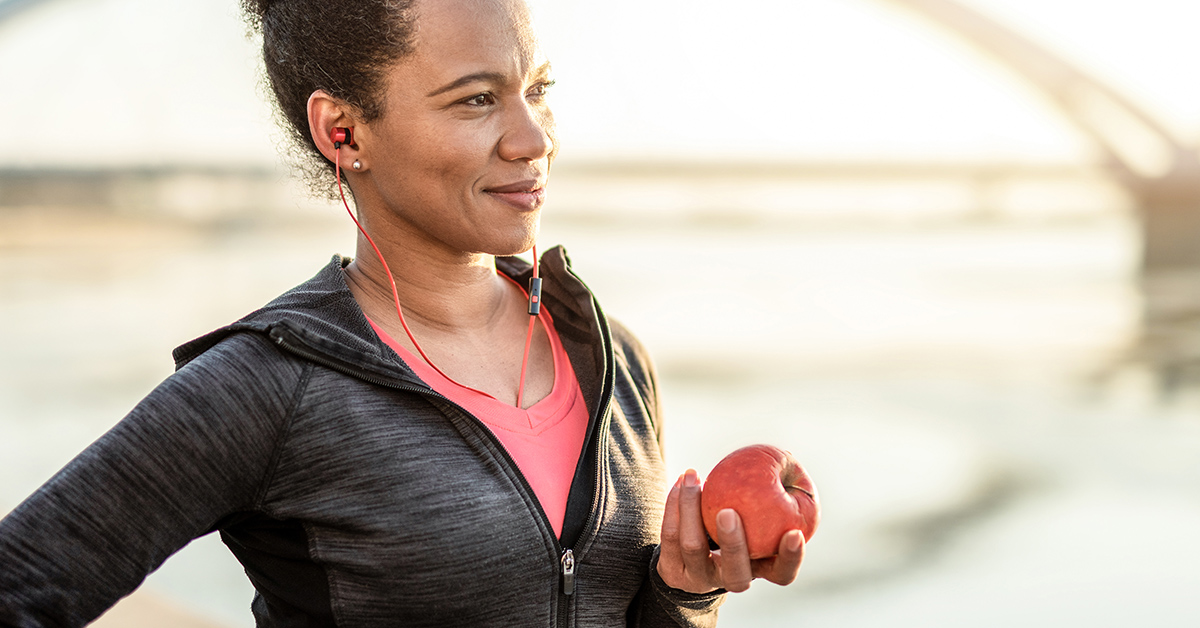 A woman eating an apple after exercising to help lower her cholesterol.
