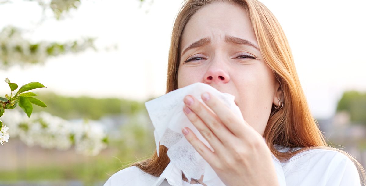 A woman using a tissue to cover her sneeze.