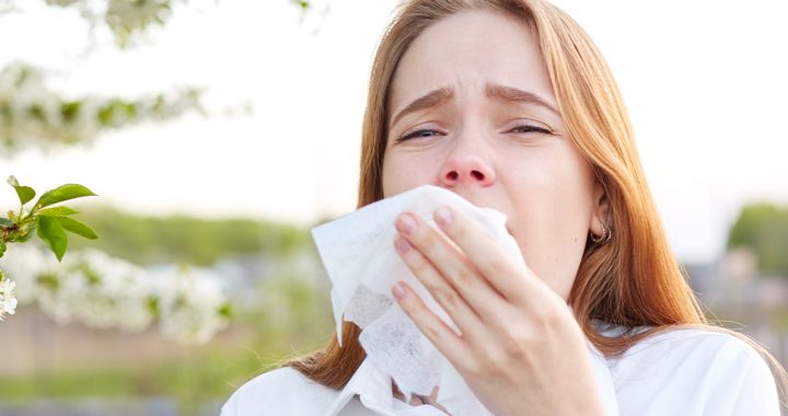 A woman using a tissue to cover her sneeze.