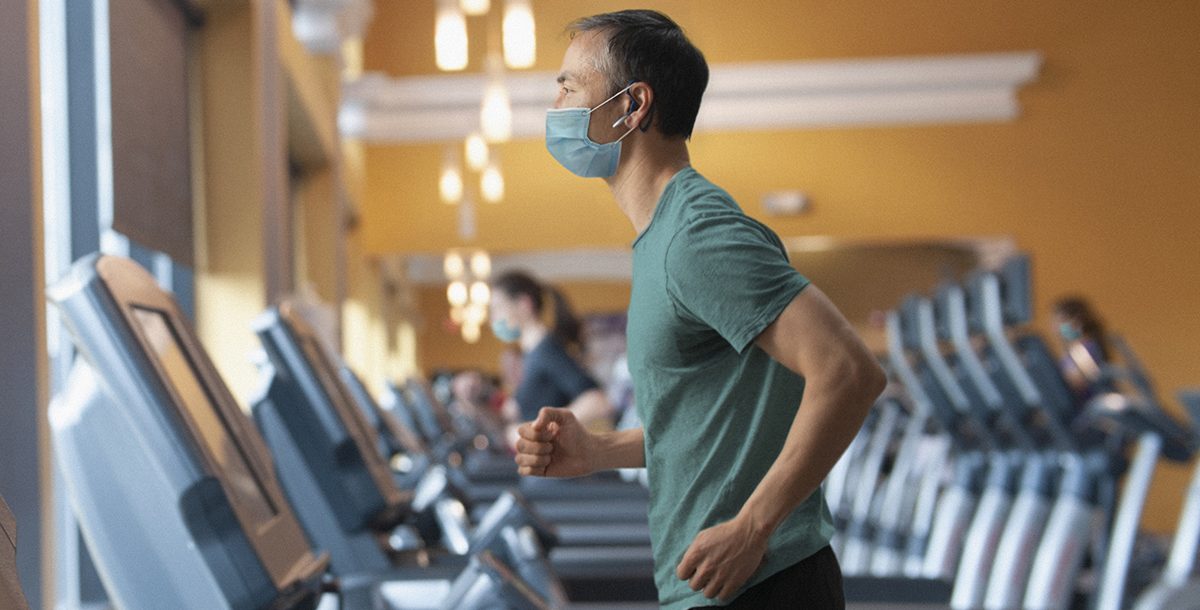 A man working out at the gym while wearing a face mask.