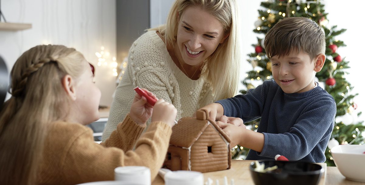A mom decorating a gingerbread house with her kids.