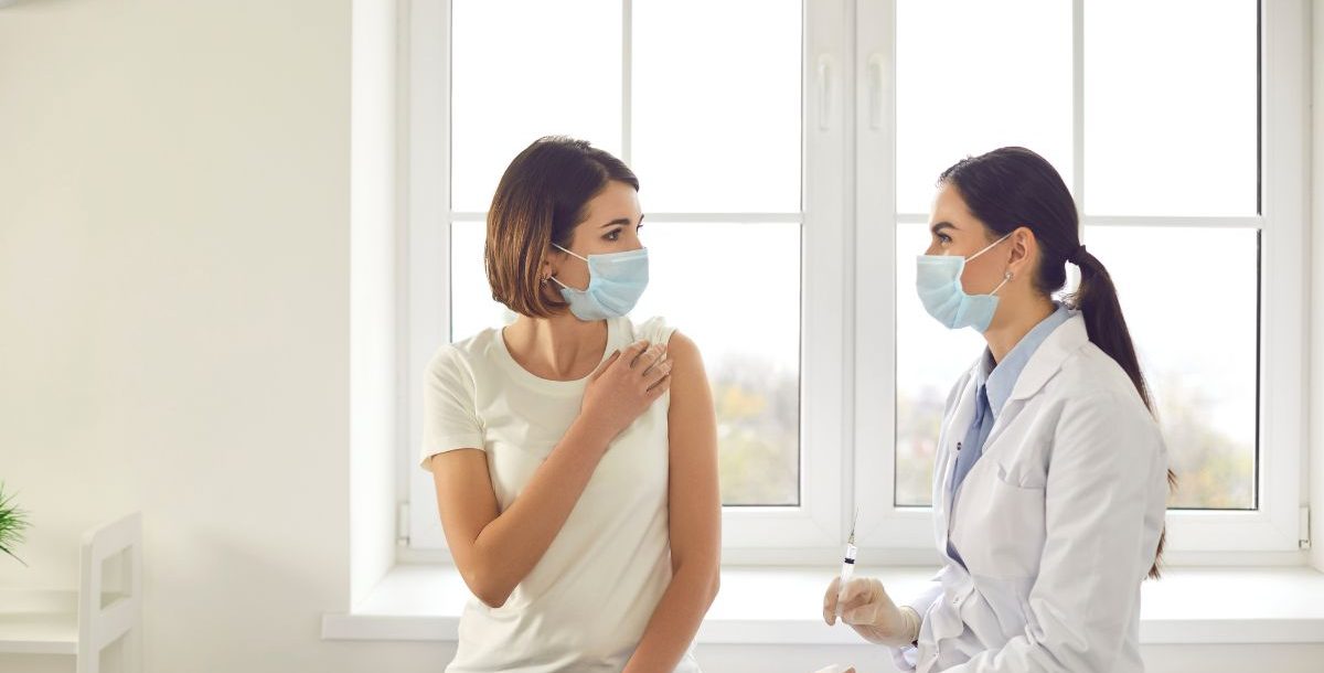 Woman with mask on prepares to receive a shot as part of rabies treatment from a doctor.
