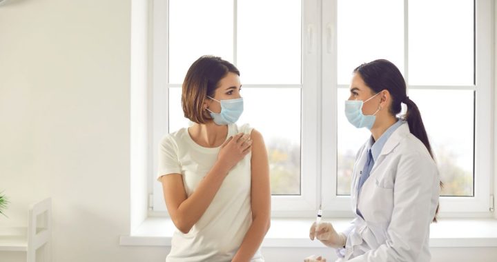 Woman with mask on prepares to receive a shot as part of rabies treatment from a doctor.